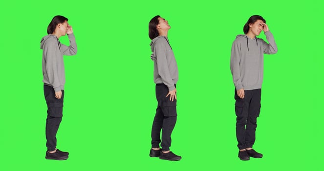 Sick man dealing with painful migraine, rubbing temples and feeling worried about bad headache. Young person being in pain, ill adult with the flu over full body greenscreen in studio. photo