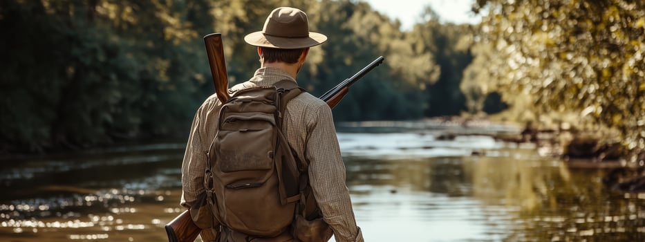 A hunter prepares for adventure along a tranquil riverbank surrounded by lush greenery on a sunny day photo