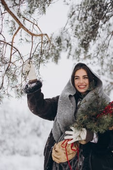 Portrait of happy pretty woman holding winter pine bouquet and posing in snowy forest photo