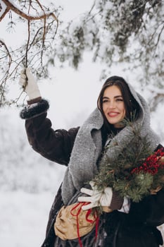 Portrait of happy pretty woman holding winter pine bouquet and posing in snowy forest photo