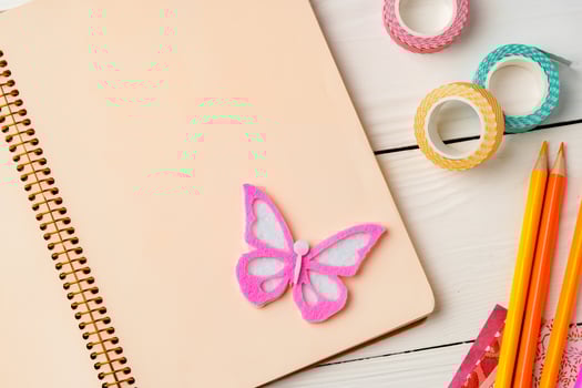 Colorful stationery arrangement with a butterfly sticker on a blank notebook at a wooden table in natural light photo