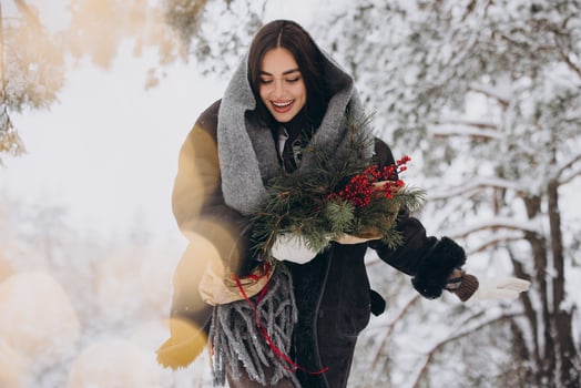 Portrait of happy pretty woman holding winter pine bouquet and posing in snowy forest photo