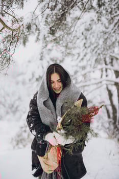 Portrait of happy pretty woman holding winter pine bouquet and posing in snowy forest photo