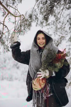 Portrait of happy pretty woman holding winter pine bouquet and posing in snowy forest photo