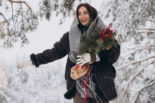 Portrait of happy pretty woman holding winter pine bouquet and posing in snowy forest photo