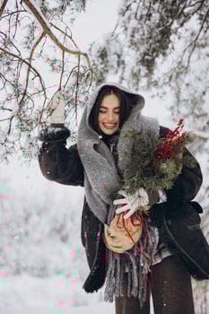 Portrait of happy pretty woman holding winter pine bouquet and posing in snowy forest photo