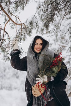 Portrait of happy pretty woman holding winter pine bouquet and posing in snowy forest photo