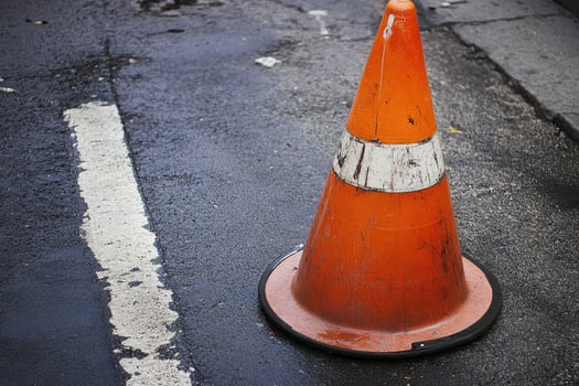 An orange traffic cone sits on a wet asphalt road. photo