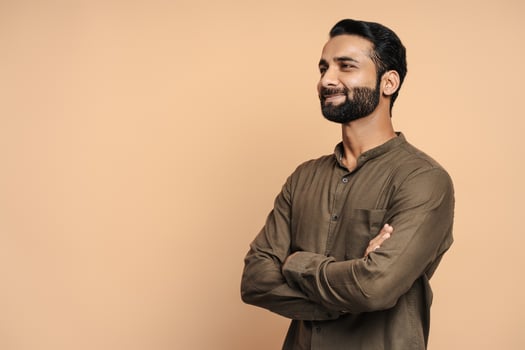 Confident indian businessman smiling with crossed arms looking away isolated on beige background photo