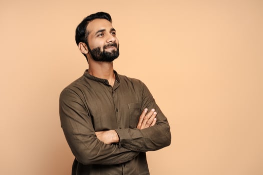 Confident indian businessman smiling and looking up with crossed arms isolated on beige background photo