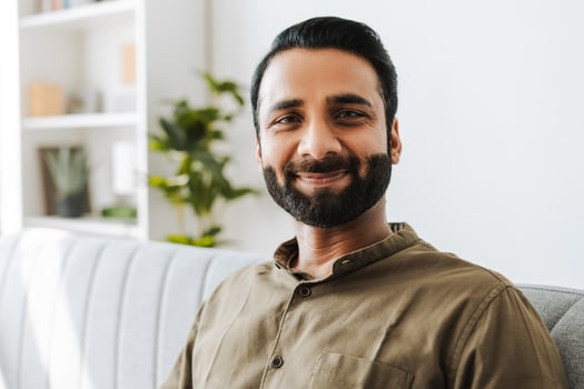 Portrait of happy, handsome indian man smiling sitting on sofa at home looking at camera photo