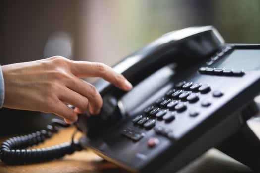 Hand holds a phone receiver, ready to dial, with blurred background photo