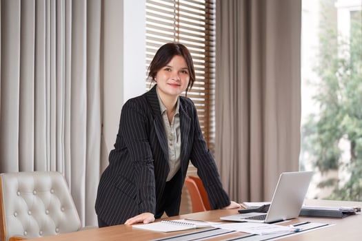 Confident Businesswoman in Modern Office Setting with Laptop and Documents on Desk, Professional Attire, Bright and Motivated Atmosphere photo