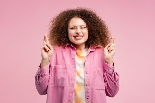 Smiling, excited, beautiful woman with curly hair, hipster with crossed fingers and closed eyes photo