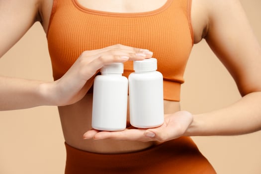 Closeup of fitness woman holding bottle with vitamins, capsules or pills and standing isolated photo