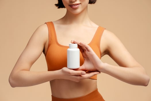 Closeup of fitness woman holding bottle with vitamins, capsules or pills and standing isolated photo