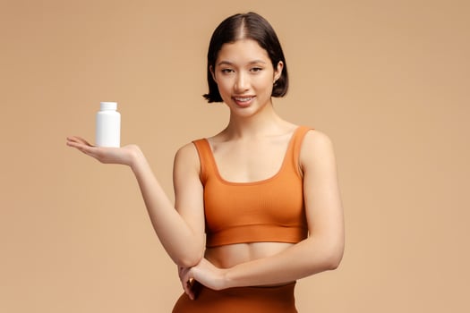 Young athletic fitness woman holding bottle with vitamins and looking at camera isolated photo