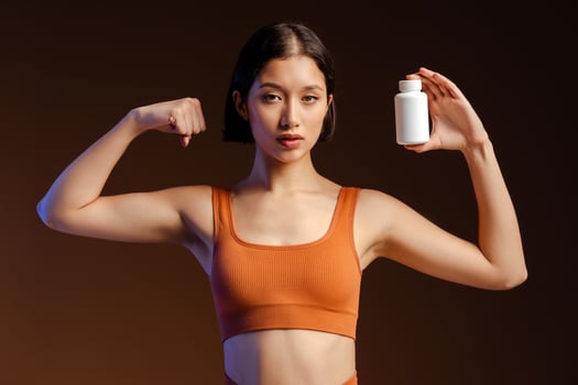 Fitness woman holding bottle with vitamins and looking at camera while standing isolated photo