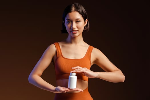Smiling woman holding bottle with vitamins and looking at camera while standing isolated photo