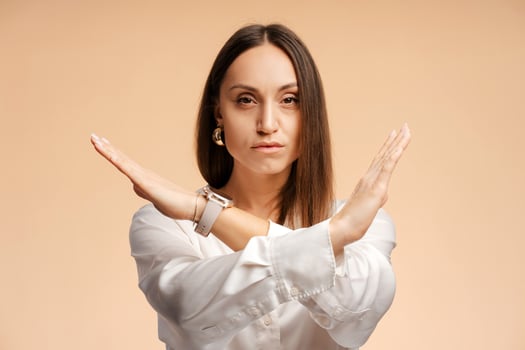 Portrait of serious young woman showing stop gesture with her palm over beige background photo