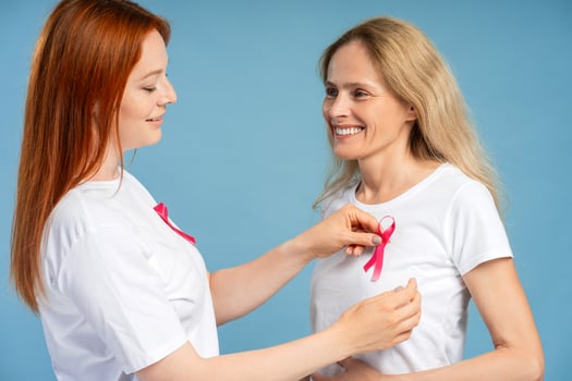Young woman pinning pink awareness ribbon on mature woman for breast cancer support photo