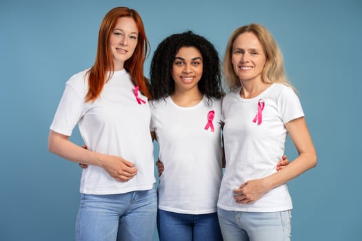 Three diverse women embrace, smiling in pink ribbons for breast cancer awareness photo
