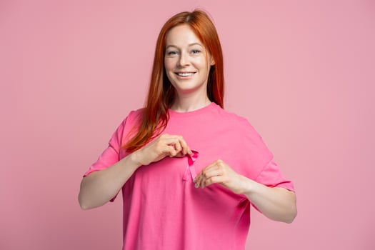 Red head woman smiling putting pink ribbon on t shirt for breast cancer awareness looking at camera photo