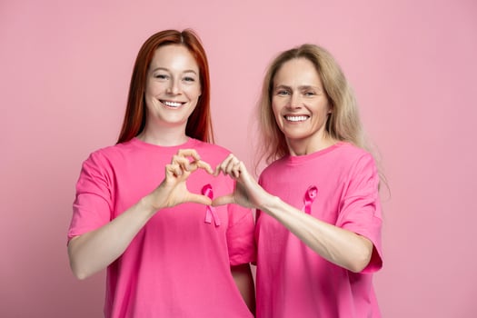 Two smiling women wearing pink t shirts with pink ribbons making heart shape with their hands photo