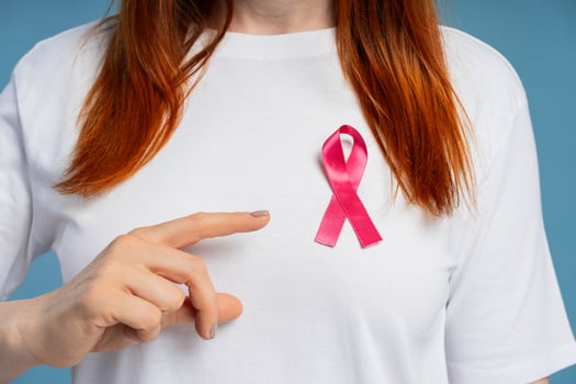 Woman pointing at pink ribbon supporting breast cancer awareness selective focus, closeup photo