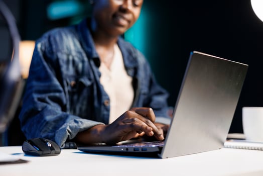 Close up of black woman at the desk typing on her personal computer, browsing the internet. African american freelancer using the laptop, answering emails, and working from home. photo