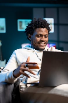 BIPOC man feeling ecstatic after receiving salary, adding payment method on website while in apartment living room. Overjoyed person delighted to do online shopping, looking to do acquisitions photo