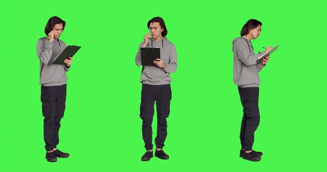 Asian adult taking notes and thinking about ideas to write on clipboard files, using papers for inspiration on camera. Person being pensive and in doubt, writing information in studio. photo