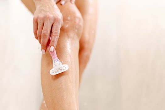 Woman shaving legs using safety razor in bathtub, enjoying depilation routine taking bath photo