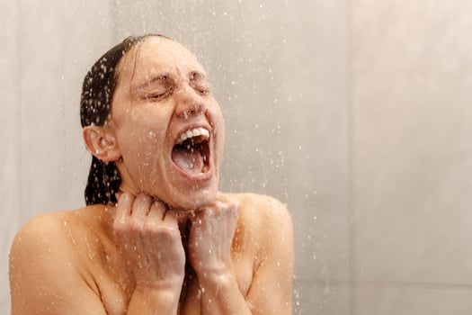 Brunette woman screaming in the shower under cold water jet photo