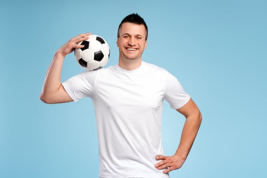 Handsome sportsman smiling and holding soccer ball on blue background photo