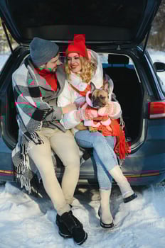 couple guy and girl sitting in car playing with dog in winter forest photo