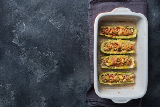 Baked stuffed zucchini boats with minced chicken mushrooms and vegetables with cheese on a baking sheet. Top view Copy space photo