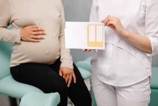 Young pregnant woman sitting on the gynecological chair during a medical consultation with gynecologist. The doctor holding the patient's medical card in his hands photo