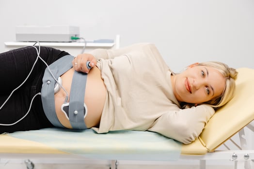 Woman pregnant checking fetal heart beat by fetal monitoring. Expectant mother with midwife adjusting sensors off cardiotocography photo