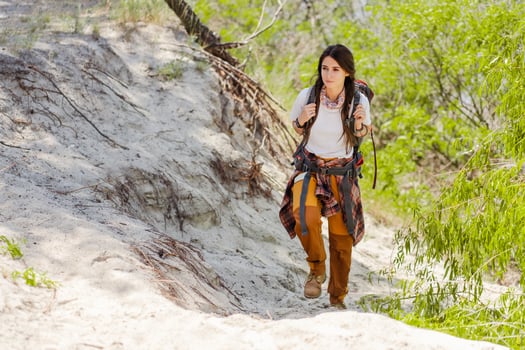 Hiker woman with backpack strolling sandy surface while hiking at warm season photo