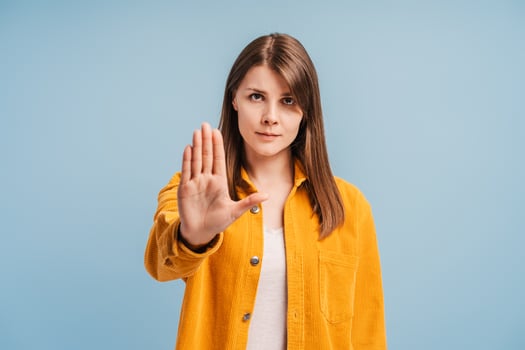 Serious attractive woman wearing stylish yellow shirt showing stop sign, looking at camera photo