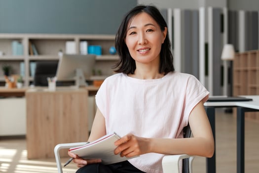 Attractive Asian businesswoman smiling while holding notebook in office photo