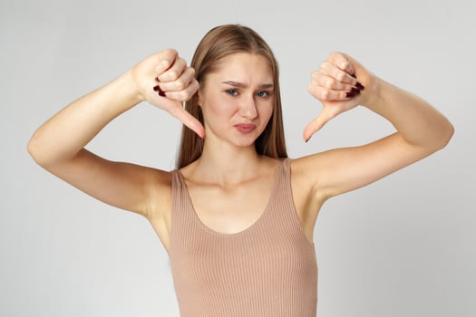 Young Woman in Casual Attire Giving Thumbs Down Gesture on Gray Background photo