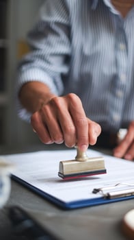 Hand stamping document on clipboard, striped shirt, blurred background focusing on action Vertical Mobile Wallpaper photo