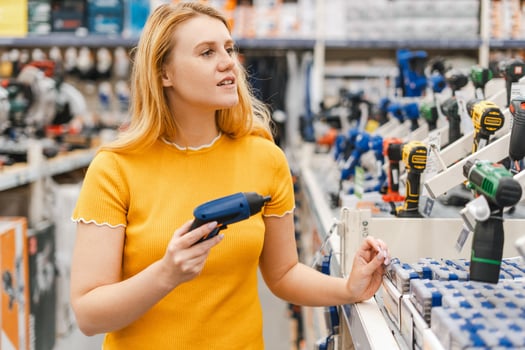 Happy young woman choosing electric screwdriver, diy, standing in construction store photo