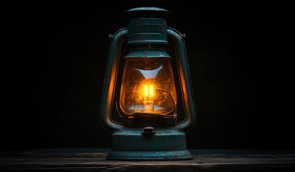 A lantern with a light inside of it is lit up. The lantern is sitting on a wooden surface photo