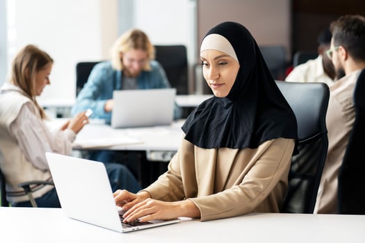 Muslim businesswoman working on laptop in busy office photo