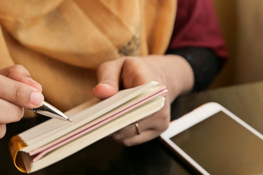 A woman is writing in her notebook while seated at a table, with her smartphone nearby photo