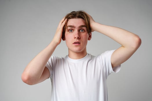 Young Man With Shocked Expression Holding Head Against a Gray Background photo