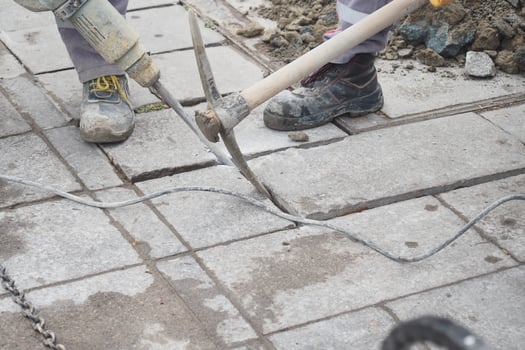A construction worker is currently using an electric jackhammer to break up pavement tiles photo